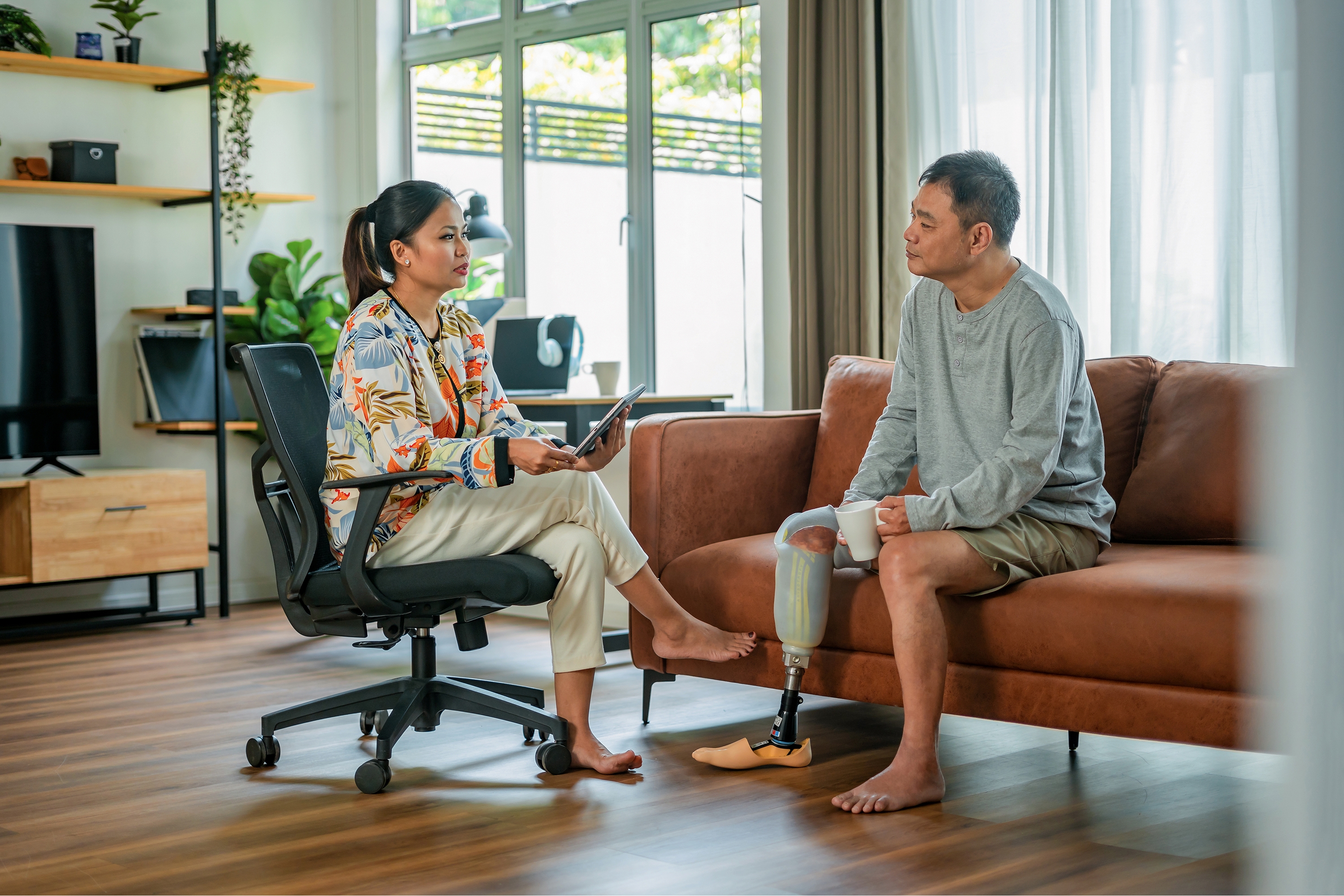 female psychologist discussing problems with amputated man on sofa during therapy session at comfortable office.
